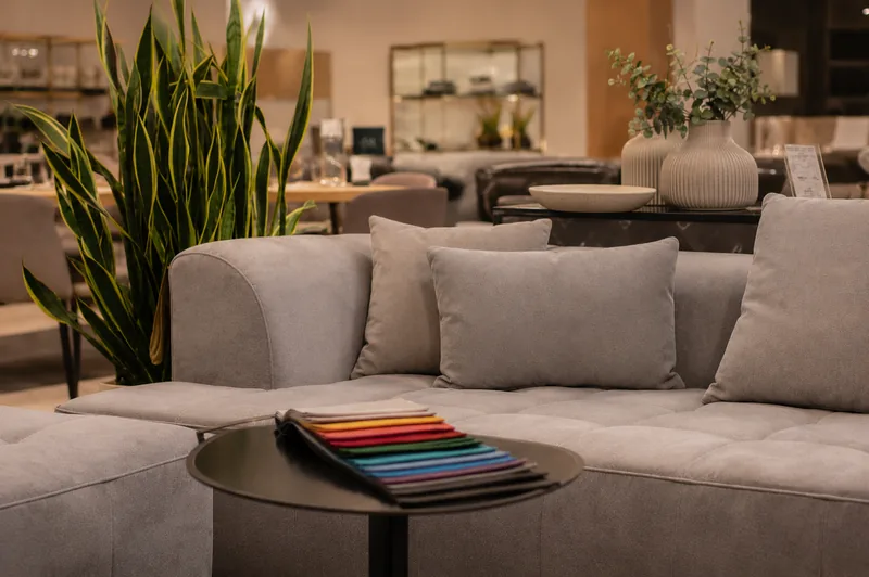 Bogenhanke und Eukalyptusgrün in Vasen als natürliche Akzente zwischen hellen Sofas – umgesetzte Innenraumbegrünung im Showroom